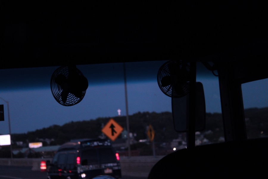 Silhouetted fans on a bus dashboard frame a highway at twilight.